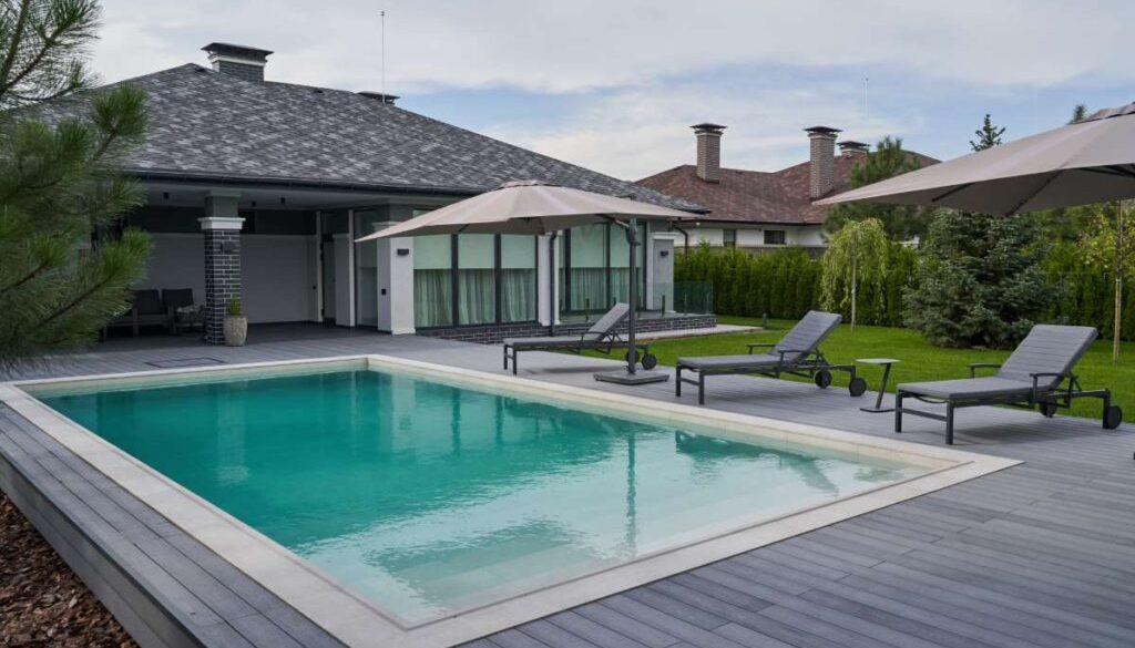 wooden-lounge-chairs-modern-villa-pool-deck-light-blue-water-swimming-pool-luxurious-mansion-with-chairs-around-it-modern-house-background_0x800