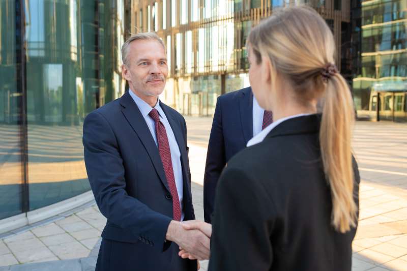confident-business-partners-standing-near-office-buildings-shaking-hands-meeting-talking-city-contract-discussion-partnership-concept_800x600