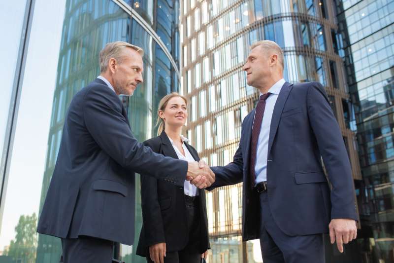 confident-middle-aged-businessmen-greeting-each-other-handshaking-successful-content-young-businesswoman-standing-near-them-smiling-building-background-teamwork-partnership-concept_800x600 confident-middle-aged-businessmen-greeting-each-other-handshaking-successful-content-young-businesswoman-standing-near-them-smiling-building-background-teamwork-partnership-concept_800x600