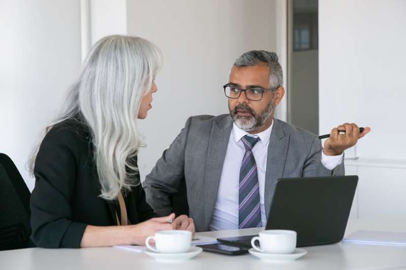 couple-serious-colleagues-sitting-table-with-laptop-documents-cups-coffee-talking-medium-shot-teamwork-communication-concept_800x600