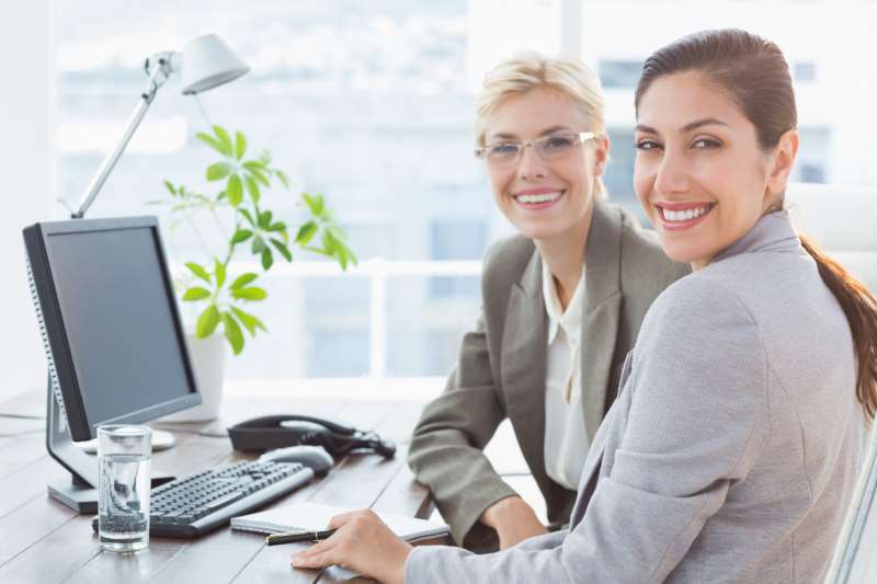 smiling-businesswomen-looking-camera-working-together_800x600