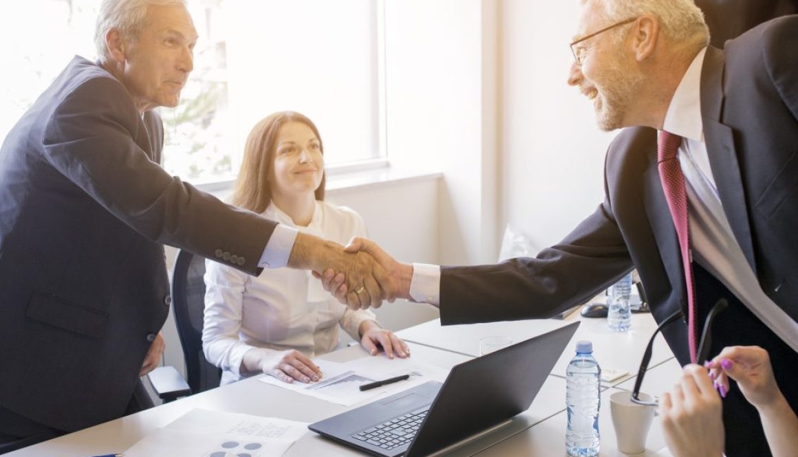 smiling-woman-looking-two-senior-businessman-shaking-hands