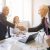 smiling-woman-looking-two-senior-businessman-shaking-hands